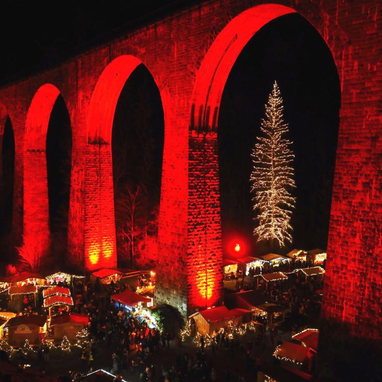 Ein beleuchteter Steinbogenviadukt bei Nacht mit einem großen festlich beleuchteten Weihnachtsbaum.