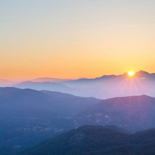 Sonnenaufgang über mehreren Schichten von blauen Bergen, die in den Nebel übergehen.